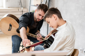 Adult man explains his son, who learn to play guitar, how to play studied chord correctly....