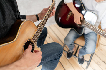Two boys of different ages sitting with guitar in hands and playing it