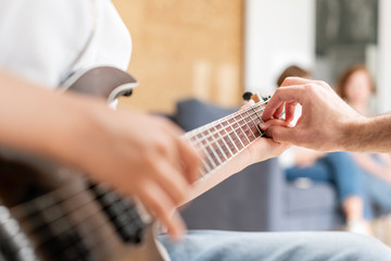 Young boy moves his hand along guitar strings while his father helps boy to take chords