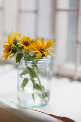 A bouquet of yellow flowers stands in a glass jar on the window.