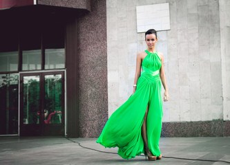 elegant woman in green dress posing against a concrete wall