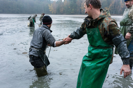 Fisherman helping another man trawling in the net at fishpond
