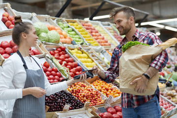 Side view portrait of handsome young man paying via smartphone at farmers market, copy space