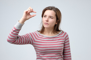 Caucasian young woman showing something small and tiny with gesture and looking puzzled. Small prise or salary concept.