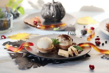 Halloween treat, autumn leaves and dessert with chocolate, ice cream and jelly worms on a wooden table