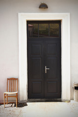 Fototapeta na wymiar Old wooden chair in a yard near the black entrance door