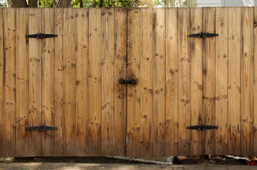 Wooden plank fence with closed gate door with black iron details and lock bolt