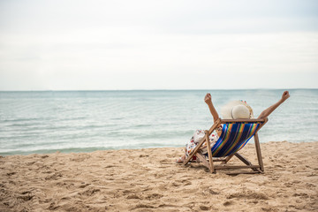 Summer beach vacation concept, Happy young Asian woman with hat relaxing on beach chair and raised hands up.