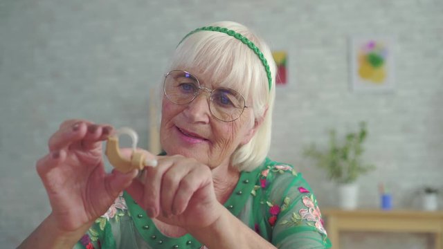 old woman holds and consider a hearing aid sitting