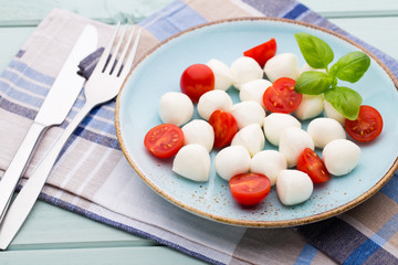 Delicious caprese salad with ripe cherry tomatoes and mini mozzarella cheese balls with fresh basil leaves.