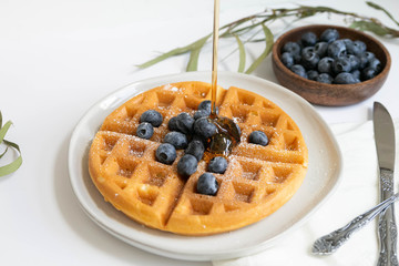Maple Syrup pouring on Belgian waffle with blueberries, Dusted with Powdered Sugar, White Background, Copy Space