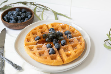 Maple Syrup pouring on Belgian waffle with blueberries, Dusted with Powdered Sugar, White Background, Copy Space