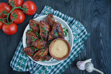 Grilled chicken wings with sauce and herbs.Baked chicken wings in pan. Dark wooden background. Space for text.