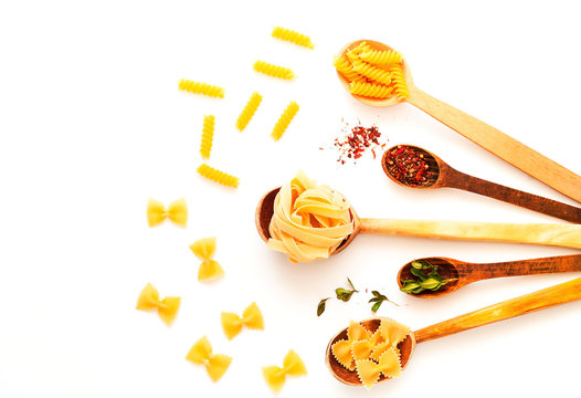 Wooden spoons with pasta and spices on white isolated background