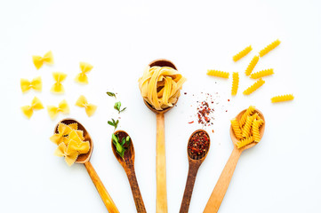 Wooden spoons with pasta and spices on white isolated background