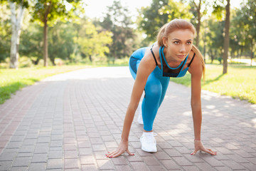 Beautiful athletic woman in starting position, ready to sprint, copy space. Attractive sportswoman working out outdoors in the park