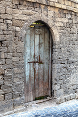 An old fence of stone blocks, with a locked, arched wooden door