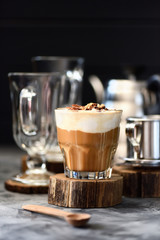 Vietnamese drip coffee with whipped coconut cream, chocolate and nuts in glass on wood slab on dark background copy space