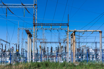 The poles and wires of elecric substation on the background of blue sky in the sunny summer weather