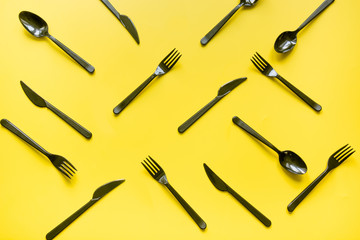 Disposable picnic black knife and forks in diagonal on yellow. Top view. Flat lay.