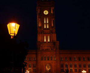 Fototapeta na wymiar View of the Red Town Hall in the center of Berlin at night. In the foreground is a historic Berlin lantern, which is not in focus.