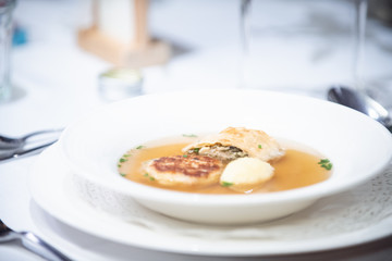 Suppe in einem weißen Porzelan Teller auf einem weiß gedeckten Tisch.
