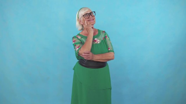 Pensive old woman stands on a blue background