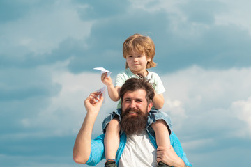 Fathers day. Family Time. Parenting. Happy father giving son back ride on sky in summer. Happy child playing with toy paper plane against summer sky background.