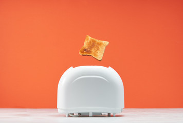 Roasted toast bread popping up of toaster with blue wall, front view