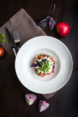 Salad with arugula, tomatoes, onions, veal, beets. Brown tablecloth, fork and spoon, food composition on the dark wooden table. Top view