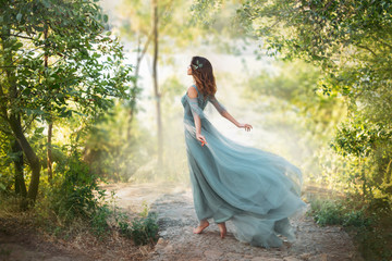 fairy-tale princess in light summer blue turquoise dress on wide path and walks towards wind, graceful dancing girl in image of flower with flying long hem of dress, nymph of bright green forest