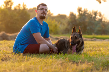View on a man and a german shepherd dog sitting on the green grass