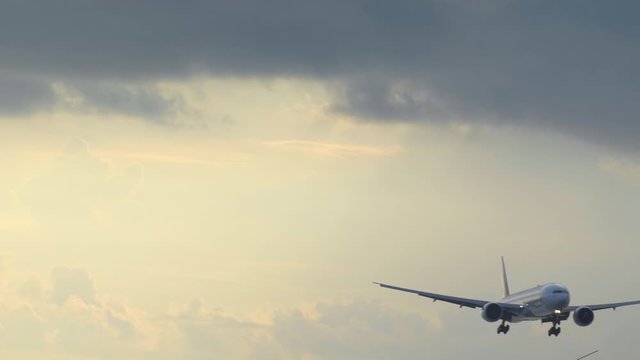 Close up of big airplane is landing in yellow sunset sky with dramatic clouds