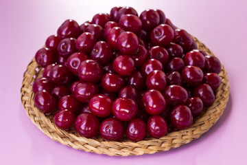 Cherry berries on a plate of wicker straws. Pink background