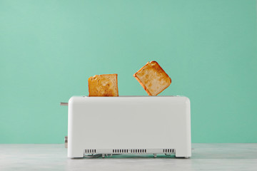 Roasted toast bread popping up of toaster with green wall