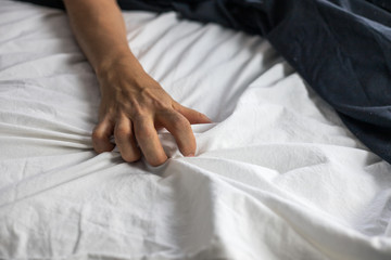 Close up detail of a women’s hand grabbing on to the bed sheets, intimacy, love, erotic concept