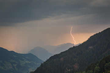 Lightning bolt strikes in a valley from an alpine evening thunderstorm