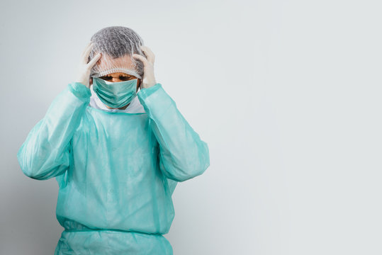 Headache of a surgeon, a doctor. A man wearing a green surgical apron and a face mask on a bright background is holding his head. Medical and pharmaceutical concept. Health problems before surgery.