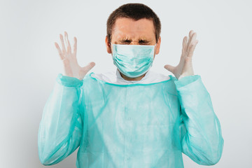 Angry and frustrated surgeon after surgery dressed in a green surgical apron and face mask on a light background. Medical and pharmaceutical concept. Failure of surgery, anger, medical errors.