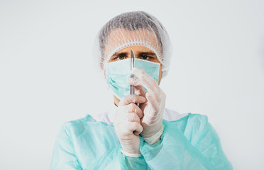 Surgeon holds scalpel dressed in a green surgical apron and mask on light background. Medical and pharmaceutical concept. Scalpel surgeon's scissors, just before surgery. Responsible work of surgeon.