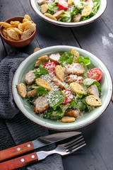 Caesar salad with fried chicken, parmesan and croutons on a dark rustic background. Vertical shot