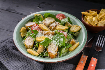Close-up Caesar salad with fried chicken, parmesan and croutons on a dark rustic background. Horizontal shot