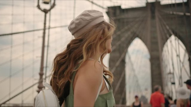 French lady walks by Brooklyn Bridge and enjoys it, first time in New York, moment from tourist's life, visiting a destination, feeling happy.