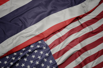 waving colorful flag of united states of america and national flag of thailand.