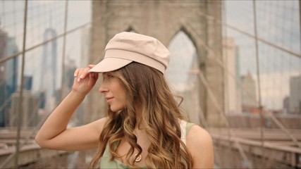 French lady walks by Brooklyn Bridge and enjoys it, first time in New York, moment from tourist's life, visiting a destination, feeling happy.