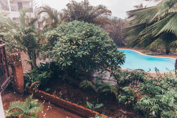 Fototapeta na wymiar Tropical rain at the hotel territory with wooden villas,pool and green palms