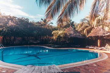 Beautiful clean blue pool and deck chair surrounded by palm trees in the tropical island