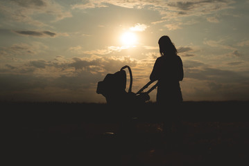 Fototapeta na wymiar Silhouette of young mother and her child in a baby carriage at the sunset outdoor.