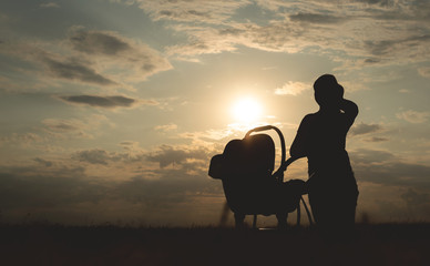 Fototapeta na wymiar Silhouette of young mother and her child in a baby carriage at the sunset outdoor.