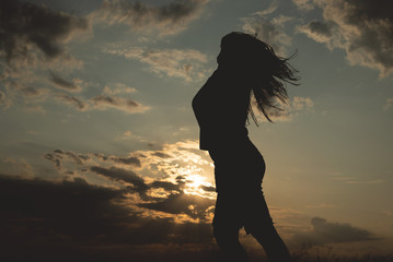 Silhouette of young dancing woman in sunset rays.